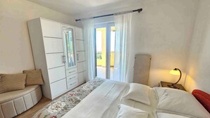 Quarto com cama, guarda-roupa, mesa de cabeceira com abajur e vista para o exterior.