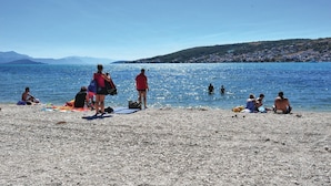 Una playa de guijarros con gente tomando el sol y nadando.