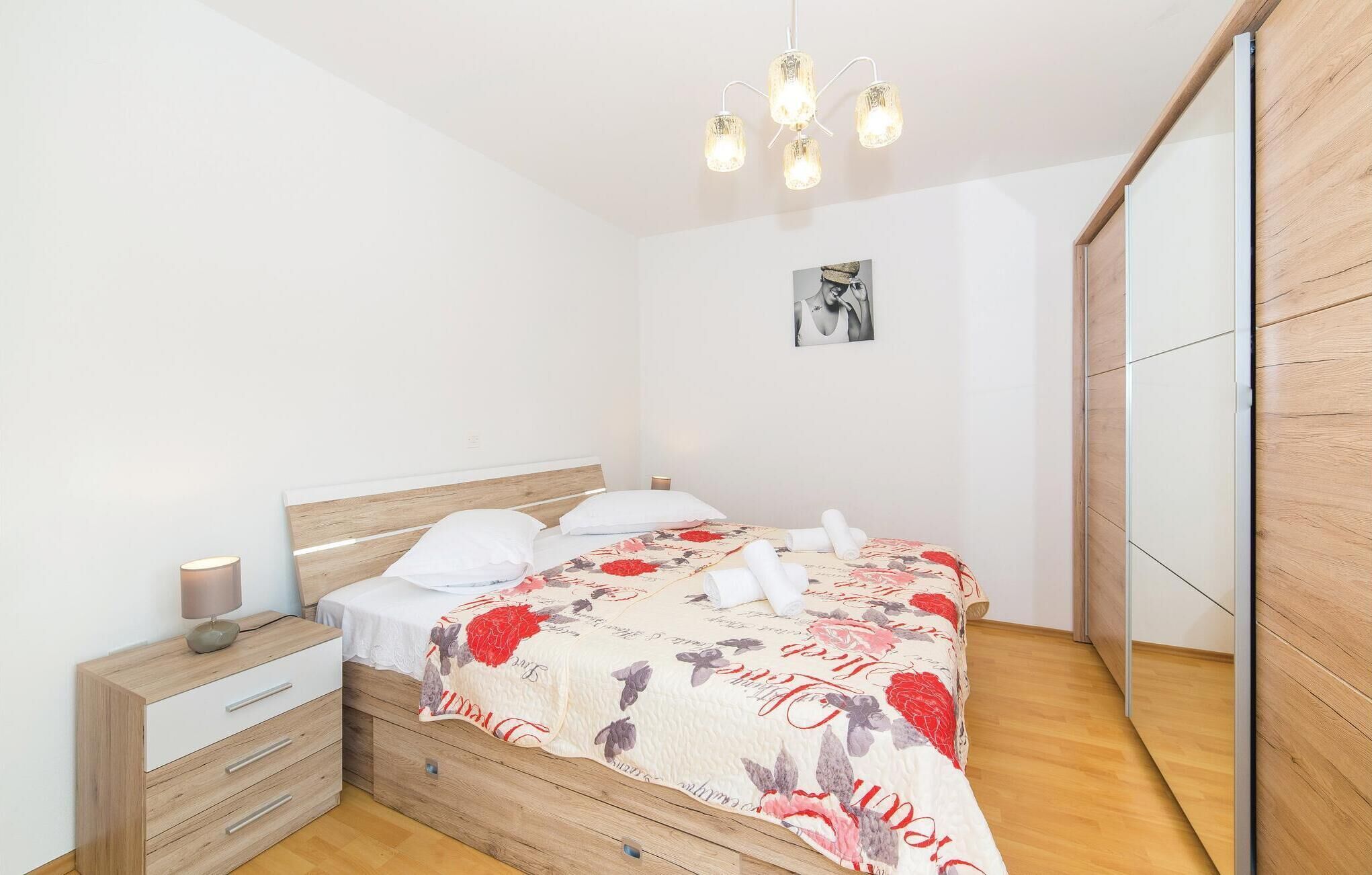 Une chambre avec un lit en bois, des oreillers blancs, une couvre-lit à motifs floraux, une table de chevet avec une lampe et un miroir sur le mur.