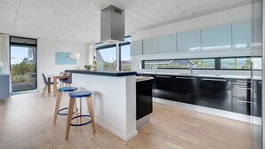 A modern kitchen with a central island, bar stools, and large windows offering a view of the outdoors. - 2 bedroom lovely home in Ulfborg (Ulfborg)