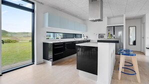 A modern kitchen with a large island, black and white cabinetry, a stainless steel refrigerator, and a view of the outdoors. - 2 bedroom lovely home in Ulfborg (Ulfborg)