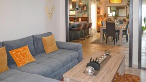 Ein modernes Wohnzimmer mit einem grauen Sofa, orangefarbenen Kissen, einem Holztisch und einer Küche im Hintergrund.