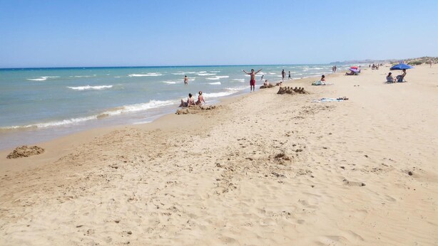 Een zandstrand met mensen die zonnen en zwemmen.