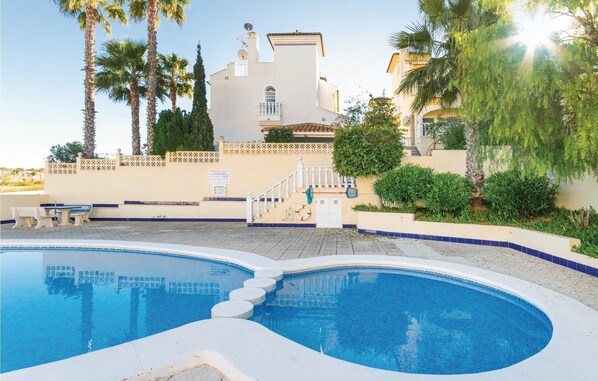 A swimming pool with a tiled deck, a white building with a balcony, and palm trees. - Stunning home in Rojales (Rojales)