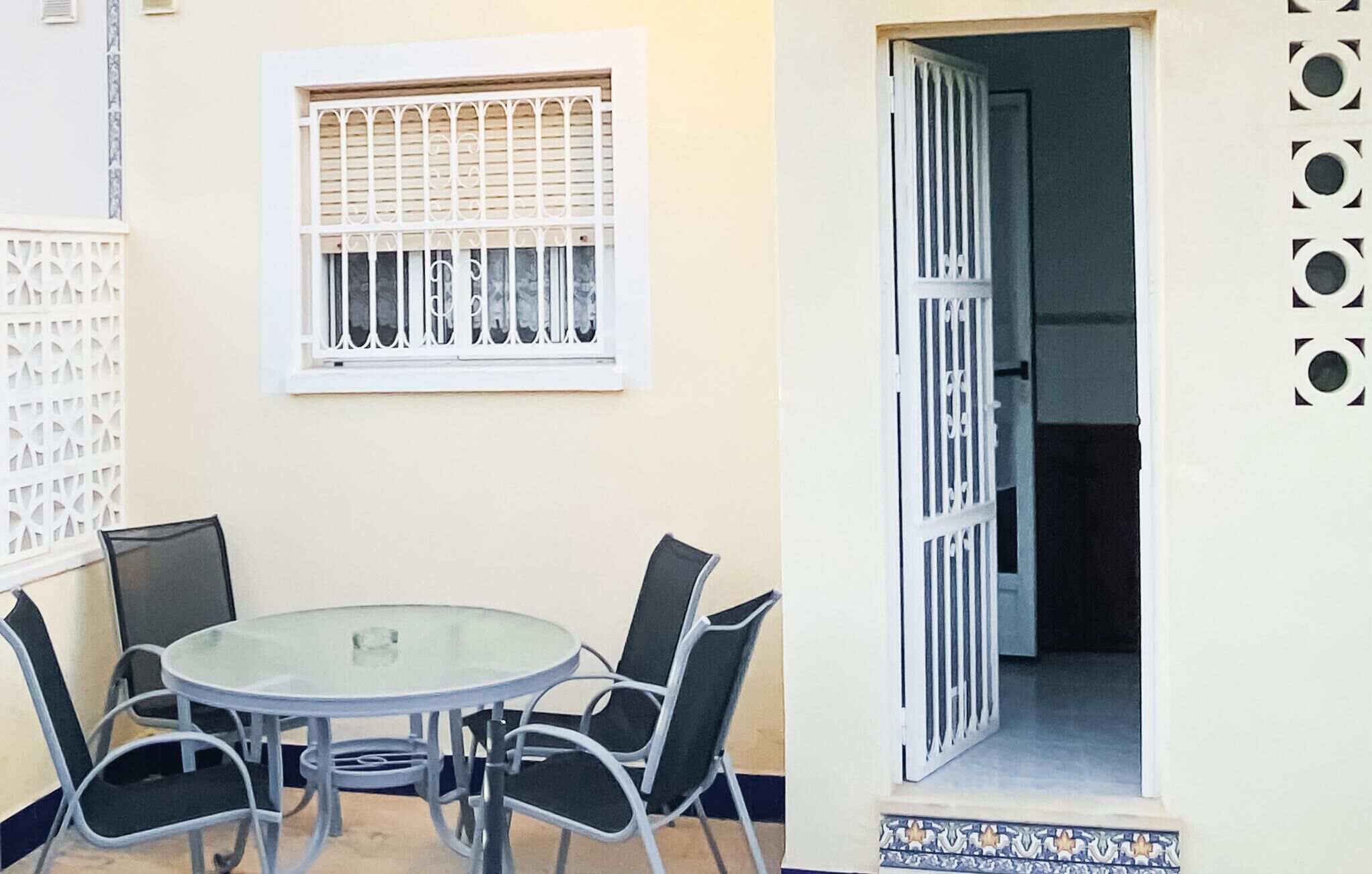 Ein runder Glastisch mit vier Stühlen, ein Fenster mit verzierten Sprossen und eine Tür mit einem gemusterten Design.