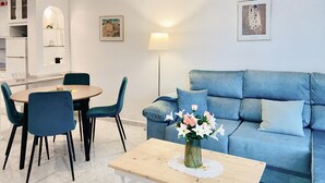 Een moderne woonkamer met een blauwe bank, blauwgroene stoelen, een houten salontafel met een bloemenvaas, en een lamp.