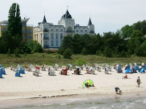 A beach with beach chairs and tents, a castle in the background, and a person walking on the sand. - Apartment Dompfaff - apartment bullfinch (Zinnowitz)