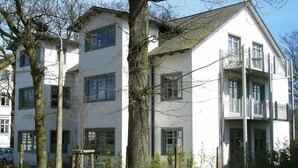 A multi-story residential building with a white facade, large windows, and a balcony on the upper floor. - Apartment Dompfaff - apartment bullfinch (Zinnowitz)
