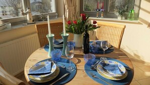A dining table set with plates, cutlery, and glasses, with a vase of flowers and candles on the windowsill. - Apartment Dompfaff - apartment bullfinch (Zinnowitz)