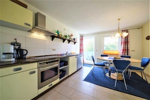Une cuisine compacte équipée d’une cuisinière, d’un four et d’un four à micro-ondes. On y trouve une table à manger avec des chaises et un tapis bleu.