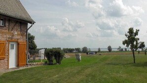 Un bâtiment en briques avec un toit en pente, un champ d’herbe et une étendue d’eau en arrière-plan.