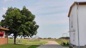 Un paysage rural avec un grand arbre, un bâtiment blanc et un champ clôturé.