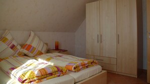 A bedroom with a bed, a wooden wardrobe, and a nightstand with a lamp. - Apartment Anna - House Uhleck (Lohme)