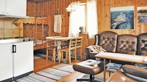 Une chambre confortable de style cabane, avec un intérieur en bois, un coin repas comprenant une table et des chaises, un canapé et une kitchenette équipée d’une cuisinière.