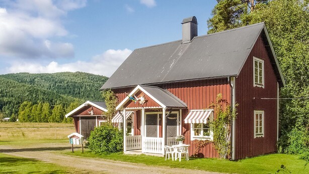 Une maison en bois rouge avec un porche, une cheminée et une petite dépendance attenante.