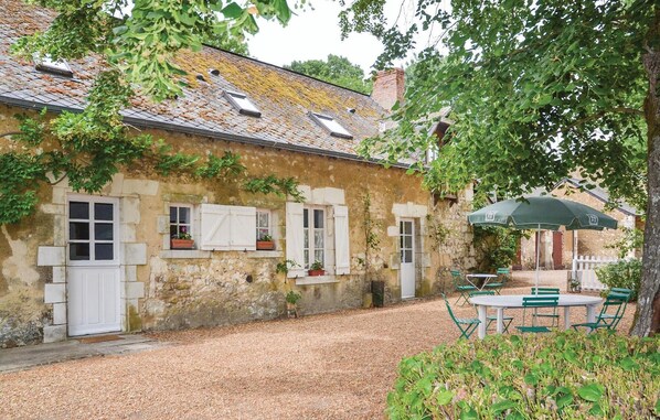 A rustic stone building with white shutters, a gravel courtyard, and outdoor seating.