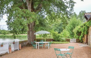 A patio area with a table and chairs, a white fence, and a tree.