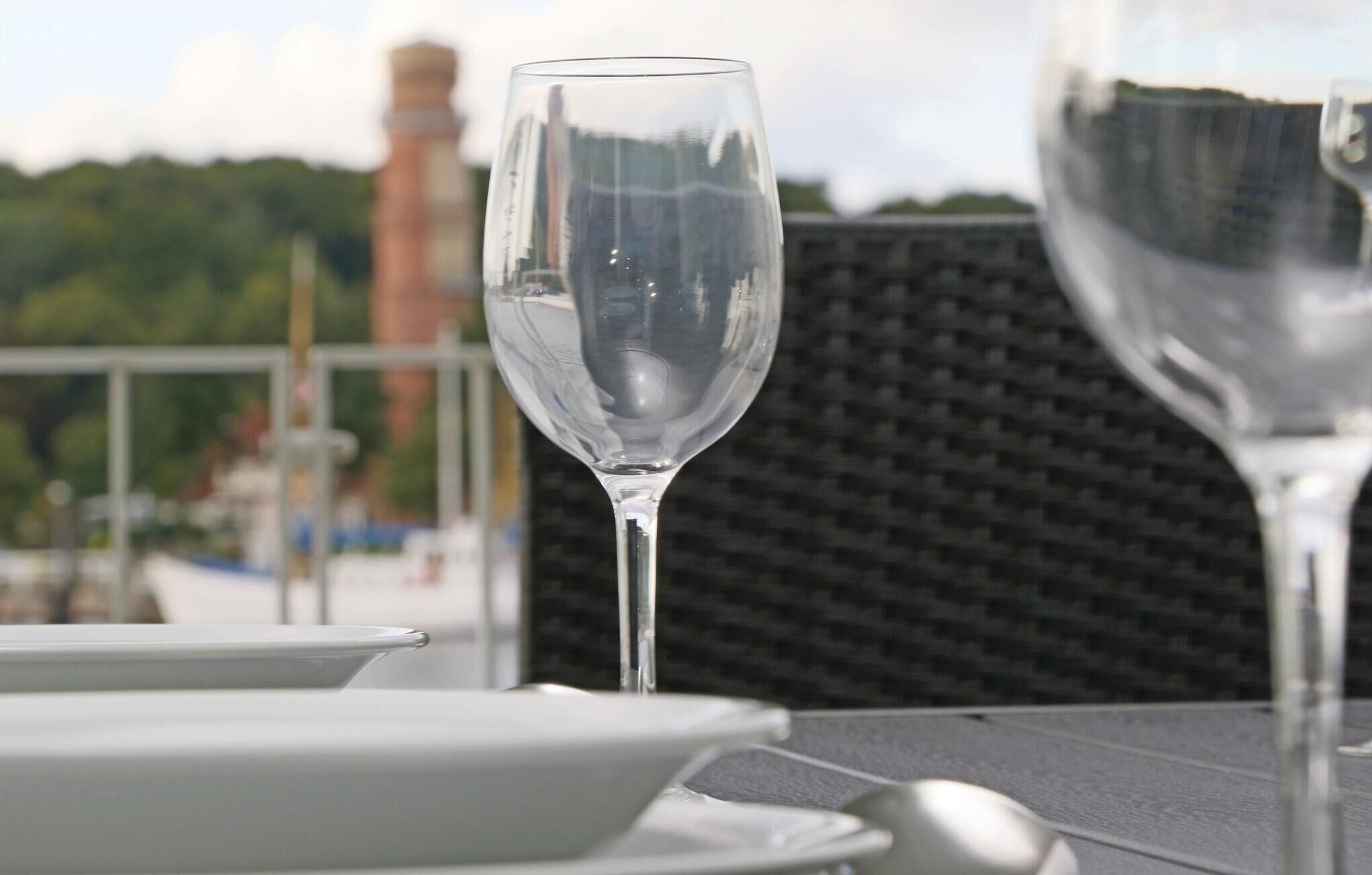 A table with a clear glass and a plate, set against a backdrop of a brick wall and greenery.
