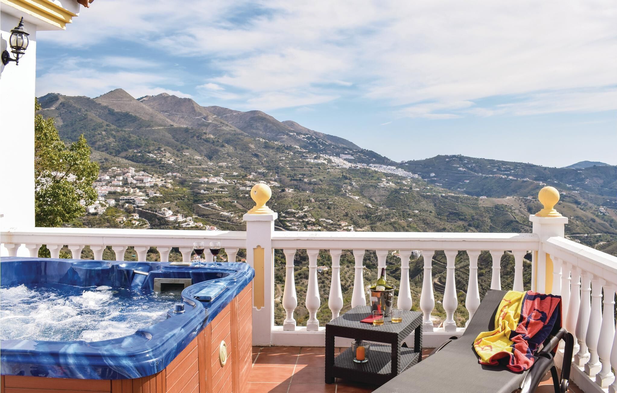 Un balcon avec un jacuzzi, une table avec une bouteille et des verres, et un fauteuil de relaxation avec une serviette.