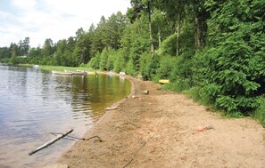 A lakeside setting with boats docked, a sandy shore, and dense forest in the background. - Beautiful home in Fristad with lake view (Fristad)