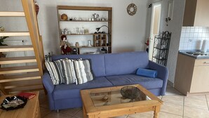 Ett vardagsrum med en blå soffa, ett soffbord i trä och ett köksområde i bakgrunden.