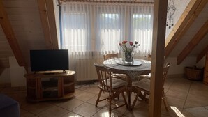 En matplats med ett runt bord, stolar, en tv och ett fönster med gardiner.