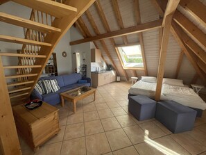A cozy attic bedroom with a loft-style staircase, a sofa, a bed, and a small kitchen area.