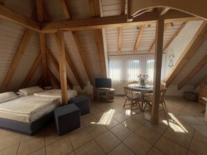 Ein gemütliches Schlafzimmer im Dachgeschoss mit einem Bett, einem kleinen Tisch und einem Fenster mit Vorhängen.