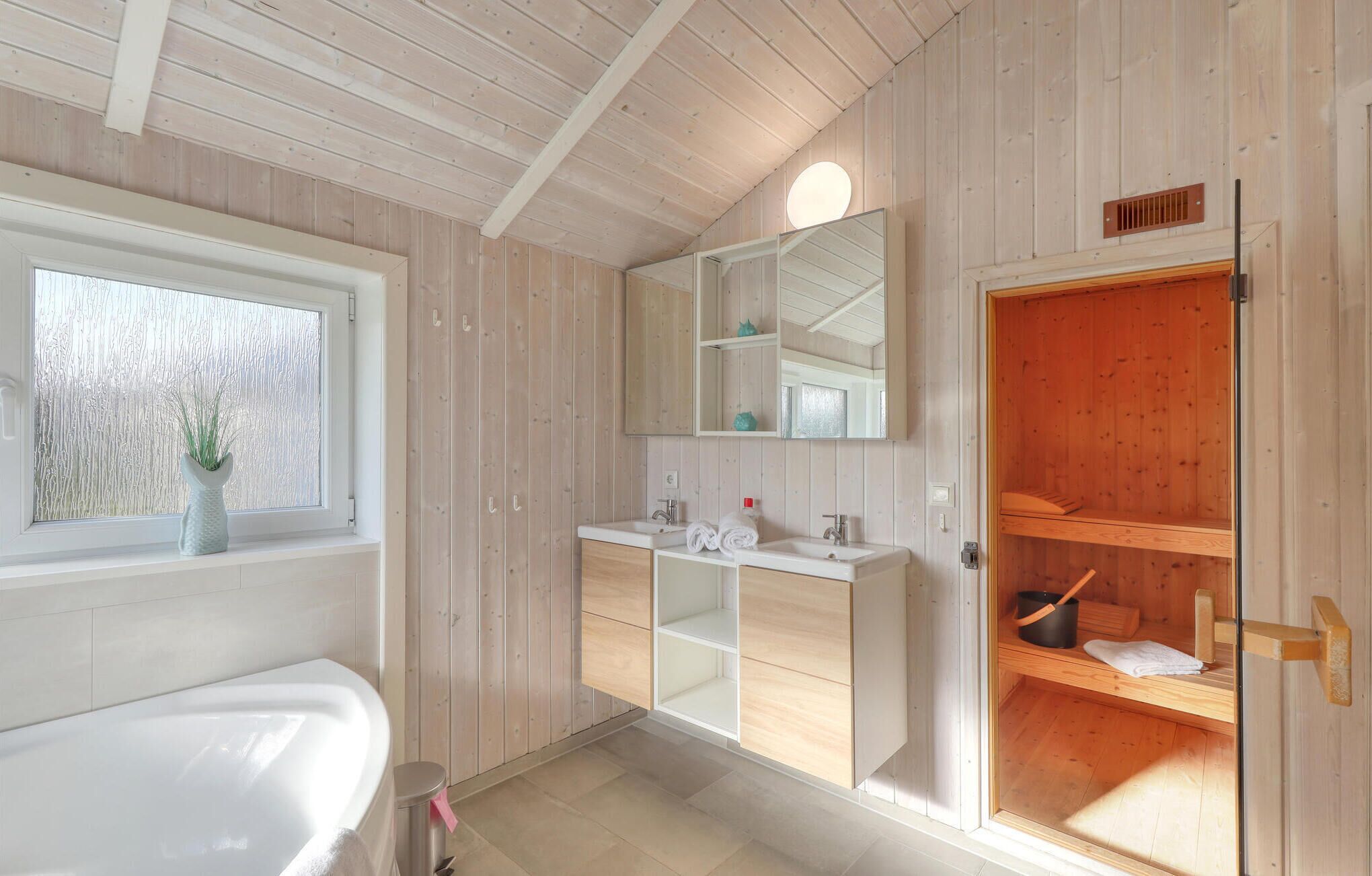 A modern bathroom with a wooden interior, a large window, a sink with a mirror, and a shower area.
