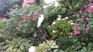 Un jardin où l’on trouve une variété de plantes et de fleurs, notamment des roses roses et une sculpture d’oiseau blanche.