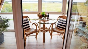 Un espace repas entièrement vitré, avec des chaises en osier et une table en verre, donnant sur un champ verdoyant.