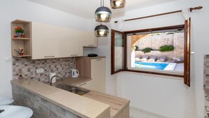 A modern kitchen with a built-in island, a window with a view of a pool, and a stone wall. - 6 bedroom accommodation in Klek (Klek)
