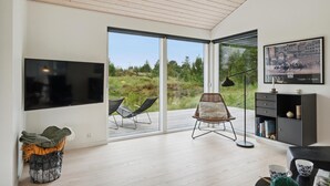 A modern living room with a large TV, a wicker chair, and a bookshelf. - Beach front home in Fjerritslev with WiFi (Fjerritslev)
