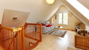 Quarto de loft acolhedor com escada de madeira, um sofá, uma mesa pequena e uma janela com relógio.