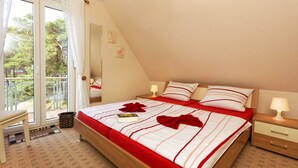 Quarto com cama, mesa de cabeceira, cadeira e varanda com vista para árvores.