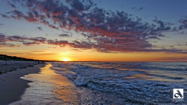 Praia ao pôr do sol, céu limpo e ondas do oceano.