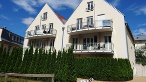 Um edifício de dois andares com varandas, telhado vermelho e uma cerca de madeira ao primeiro plano.