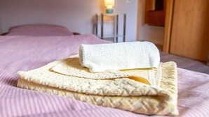 Un lit bien fait, avec une serviette blanche pliée et une serviette beige pliée posées sur une couvre-lit à rayures roses.