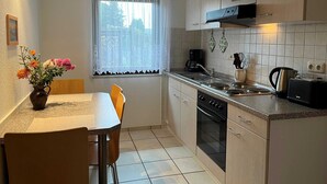 A compact kitchen with a dining area, featuring a window with sheer curtains, a coffee maker, and a toaster. - Vacation home Lorenz - Apartment 1/EG (Mölschow)