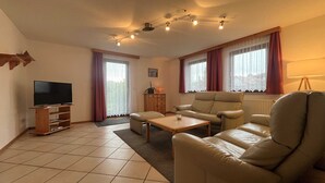 A living room with a flat-screen TV, leather sofa, wooden coffee table, and a cabinet. - Vacation home Lorenz - Apartment 1/EG (Mölschow)