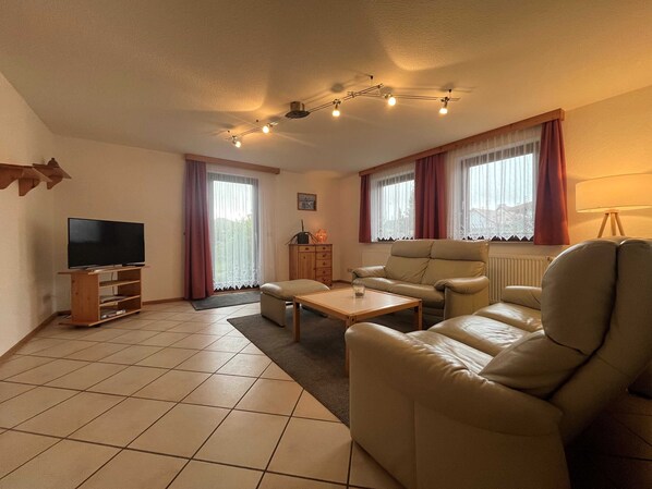A living room with a flat-screen TV, leather sofa, wooden coffee table, and a cabinet.