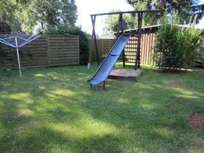 A backyard with a slide, a wooden fence, and a small garden area.