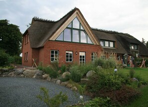 A traditional house with a steeply pitched thatched roof, large windows, and a brick exterior. - Apartment downstairs - House Goldhöft 7 (Gelting)