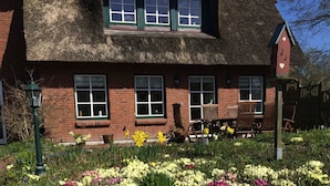 En traditionel murstensvilla med stråtækt tag, mange vinduer og en blomsterprydet have.