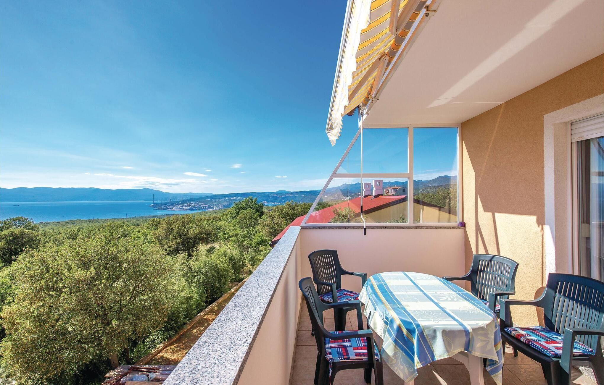 A balcony with a table and chairs, overlooking a scenic view of a coastline and hills.