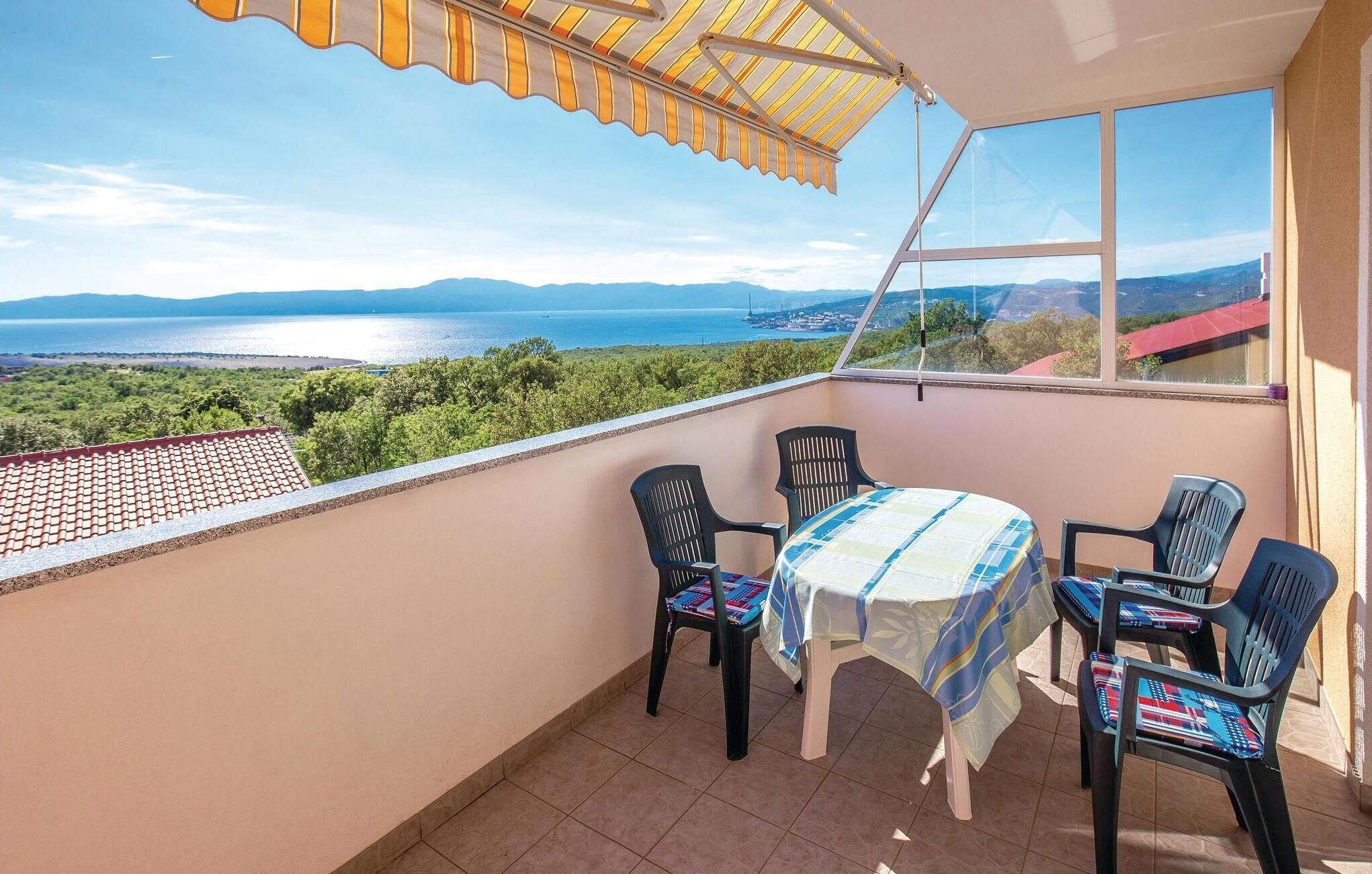 A balcony with a table and chairs, a view of the sea and mountains, and a striped awning.