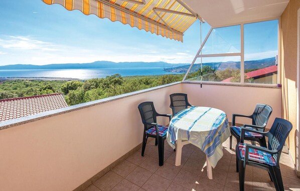 A balcony with a table and chairs, a view of the sea and mountains, and a striped awning.