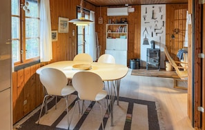 L’intérieur chaleureux d’un chalet avec une table à manger ronde, des chaises blanches, un panier en osier et un plancher en bois rustique.