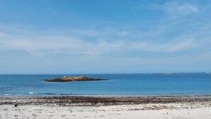 Une plage avec un ciel dégagé, une eau calme et un promontoire rocheux à l’horizon.