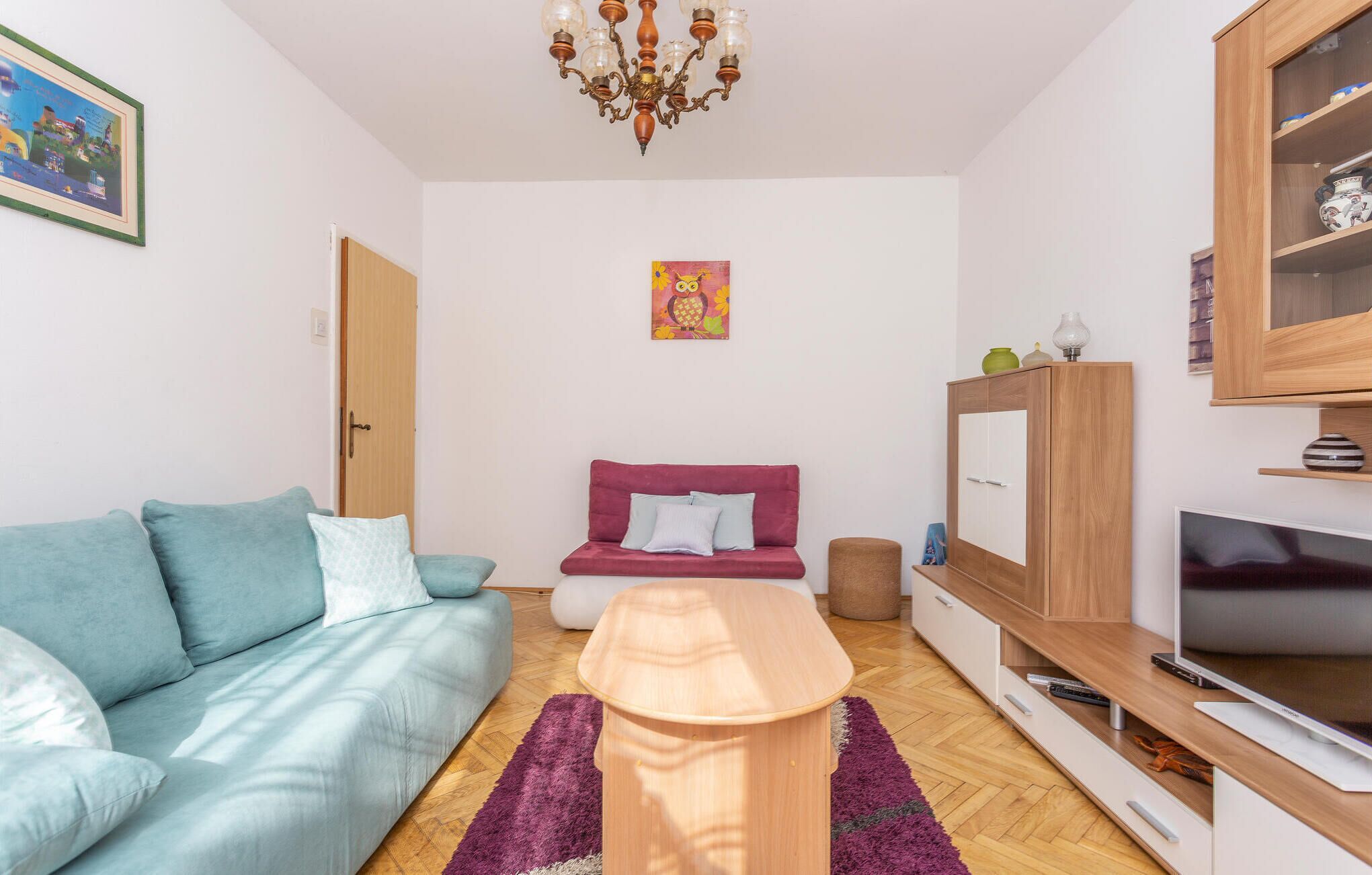 Ein modernes Wohnzimmer mit einem türkisfarbenen Sofa, einem roten Sofa, einem Holztisch, einem Fernseher und einem Schrank mit Dekorationsgegenständen.